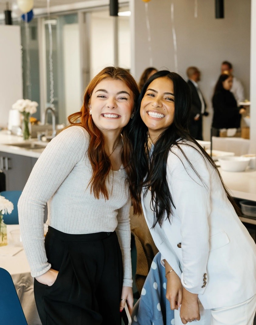 Two women smiling and leaning towards one another.